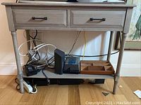 Front view of console table showing two drawers with metal handles, turned legs, and lower shelf holding miscellaneous items.