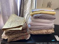 Stack of linens on a tabletop showing variety of textures and colors including cream, beige, yellow, lavender, white fabrics