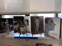 Four hardcover books displayed upright, titles related to Elizabeth Taylor and Jacqueline Kennedy, some visible wear on bindings