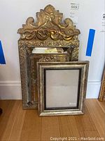 Photo showing metal Moroccan style wall mirror with cabinet and 11x14 picture frame stacked against a wall on wood floor.