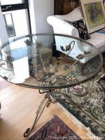 Overall view of the round glass table with wrought iron base decorated with grapevine and floral details.