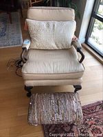 Overall view of the beige striped upholstered armchair with wooden arms and legs, ottoman in front, and throw pillow on chair.