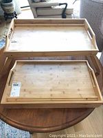 Two wooden bed trays placed on a round wooden table showing the foldable legs and flat tray surfaces.