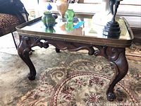 Full view of vintage square side table with carved claw foot legs and brass tray mirror top, sitting on patterned area rug.