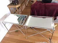 Two silver tone metal side tables with bamboo design frames and mirror tops placed on a wood floor beside a burgundy sofa and other furniture.