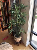 Side view of the faux bamboo plant in the planter on the wooden stand near window and room divider.