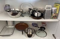 Overview of bowls, pots, pans, lids, strainer, and grater arranged on shelves
