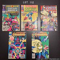 Photo showing front covers of all five comics: 2 Captain America and 3 Excalibur, spread on surface.