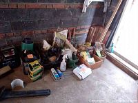 Wide shot showing various garden supplies including battery booster, broom, garden edging, small bottles and boxes, and other tools aligned against a wall.