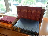 Overall view of maroon Anchor Bible Dictionary volumes, navy Story of the Bible books, Oxford Iliad, cloth-bound hardcover, and orange Cambridge handbooks on table