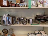 Photo of shelf showing cake plate with dome cover, tea set items, egg cups, and nested stainless steel mixing bowls.