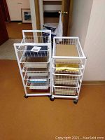 Photo of two white wire drawer carts standing side by side on caster wheels with various papers inside drawers.