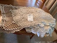 Folded off-white crochet mats and doilies laid on a wooden table with a note 'Linen' visible