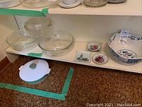 Four clear glass Pyrex casserole dishes with lids, two round candy dishes, and a large white ceramic bowl with blue floral pattern on shelf.