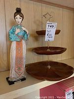 Photo of the Taiwanese doll next to the three-tier wooden cake stand on a shelf.