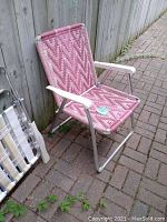 Homemade pink folding chair with white metal armrests and frame, shows wear on plastic woven straps.