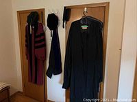 Two academic gowns, hood and headwear hanging on two doors