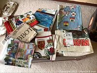 Photo showing 7 folded vintage linen souvenir tea towels with colorful designs and Canadian themes, laid out on a flat surface.