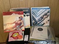 Photo showing multiple vintage vinyl LP records stacked vertically and horizontally on a black shelving unit including albums by The Beatles and The Rolling Stones; older records with worn covers visible.