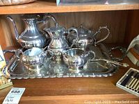 Silver plated tea and coffee set on a large tray with several pieces including teapots, creamer, sugar bowl and covered vessels.