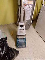 Front view showing the upright Hoover Steam Vac cleaner with beige upper body and teal base, with 'Hoover' clearly visible.