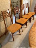 Four teak dining chairs with orange tweed seats lined up against wall