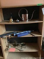 Shelving unit containing travel umbrellas, hand bells, brass watering can, and assorted brassware items.