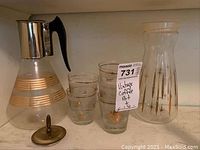 Group photo of coffee carafe with metal lid and black handle, juice carafe with starburst pattern, and four matching glasses with gold bands.