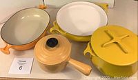 Overview of 5 items: orange Le Creuset saucepan with lid, orange oval baking dish, yellow round baking dish, yellow casserole pot with lid