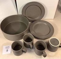 Photo shows the full dinnerware set: one large salad bowl, nine plates, and four cups in matte gray.