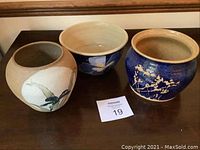 Photo showing three pottery pots arranged side by side on a wooden surface.