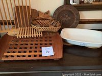 Assortment of wooden slatted trivet, wooden latticed cutting board, woven basket bowl, round carved wooden trivet, and white ceramic Corning Ware roaster dish on a dark surface