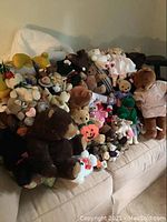 Photo showing a large assortment of teddy bears and stuffed animals arranged on a beige couch, including various Boyd's Bears and Vermont Teddy Bears mostly with tags, and some dressed in costumes.