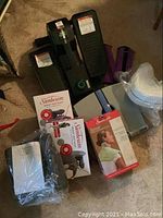 Lot viewed on carpeted floor showing black pedal exerciser, ankle weights, comfort pillows, three boxed heat wraps.