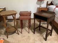 Three antique tables set on carpet: curved side table with lower shelf, two reddish nesting tables, and dark rectangular tray-top table with turned legs.