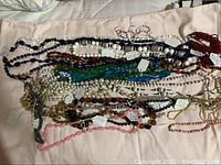 Photo showing a large assortment of vintage costume jewelry necklaces, various colors including white, navy blue, amber, green, pink, and red beads.