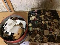 Photo of two large tins filled with assorted buttons including button cards and loose buttons.