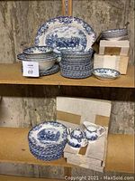 Shelves of Johnson Bros Ironstone dinnerware including plates, bowls, a large serving platter, and boxed sugar and creamer set, all in blue and white Coaching Scenes pattern.
