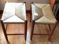 Two matched wooden stools with woven rush seats, viewed from above on wood floor.