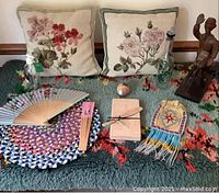 Photo of lot showing hooked rug, needlepoint pillows, carved wooden figure, beaded purse, braided mat, printed fans, small wooden box, and bottle.