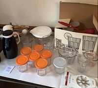 Photo of assorted vintage kitchen glassware and tools including measuring cups, jars, thermos, and sieves