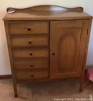 Front view of vintage wooden nursery dresser showing four drawers and one cabinet door with wooden knobs, curved top backboard, and slender legs.