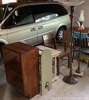 Photo showing a silver minivan in a garage with wooden furniture and two vintage floor lamps arranged in front of it