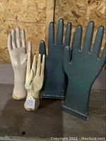 Four wooden display hands of varying sizes and colors on a wood surface against a wood panel background.