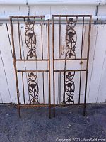Two bronze metal garden trellis panels side by side in front of white fence