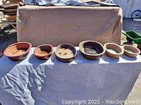 Six ceramic bonsai planters displayed in a row showing variety in shapes and sizes