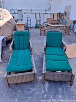 Front view of two outdoor La-Z-Boy loungers with green cushions sitting on paved ground, showing cushions and wicker detail.