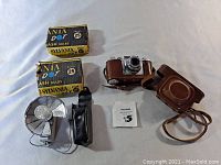 Photo showing entire set including the Ricolet camera, external flash unit with leather pouch, two unopened boxes of Sylvania flash bulbs, and the brown leather camera case with strap.