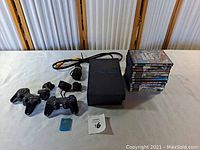 PlayStation 2 slim console with two wired controllers, power and AV cables, 8MB memory card and stack of games
