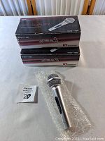 Two KY Kumyoung KYM-100 dynamic microphone boxes stacked, with one silver microphone lying in front wrapped in bubble wrap on a white surface.